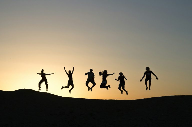Jubelnde Menschen Sechs Menschen springen ins Glück vor einem Sonnenuntergang.