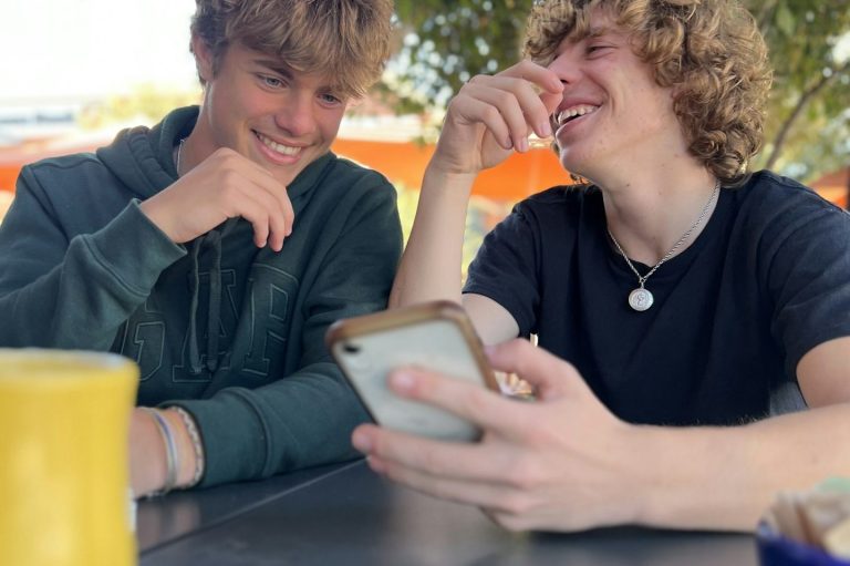 Zwei Jugendliche lachend Zwei junge Männer sitzen an einem Tisch und lachen, während sie gemeinsam aufs Handy schauen.